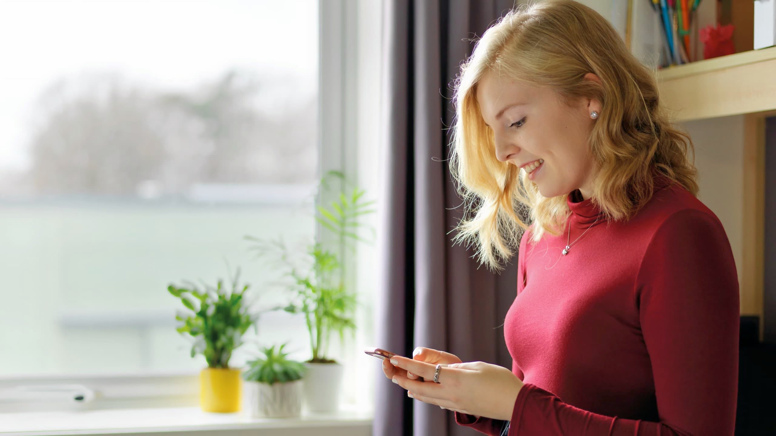 A student smiles as they use a phone in their room.