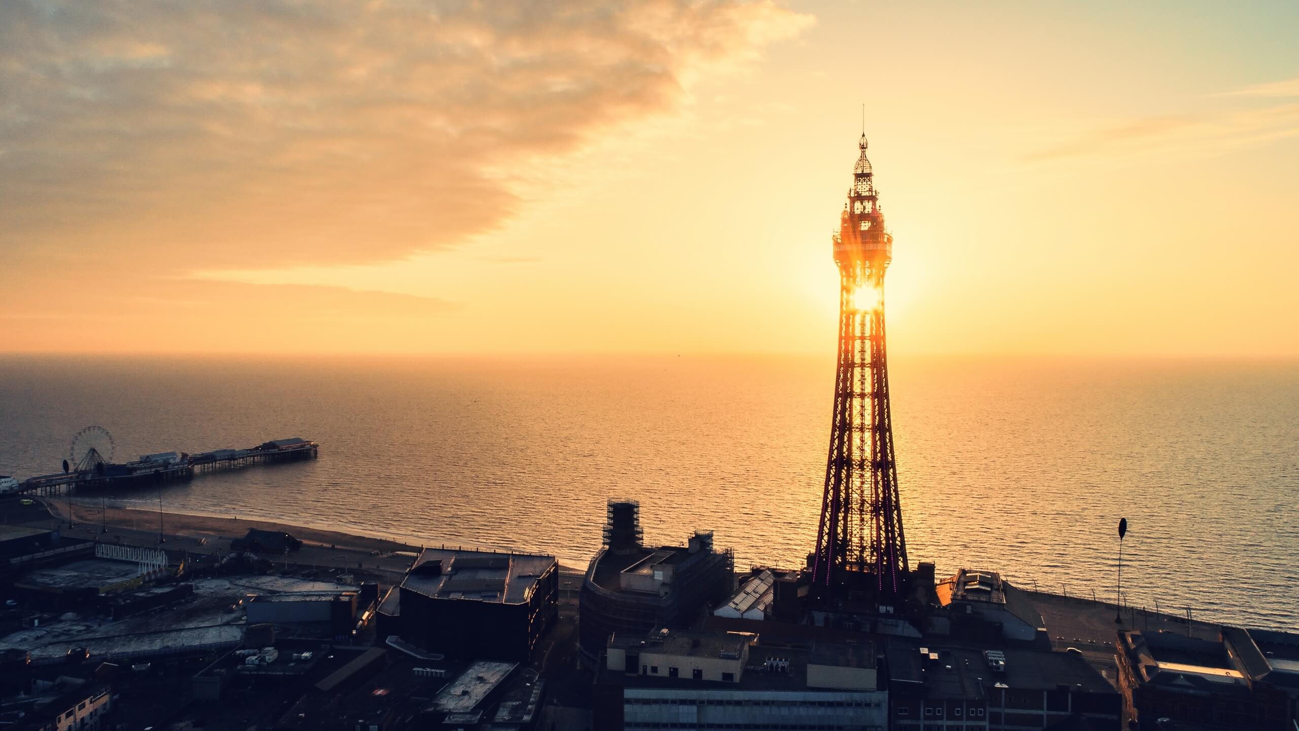 The setting sun peaks through the structure of Blackpool Tower, with the sea behind.