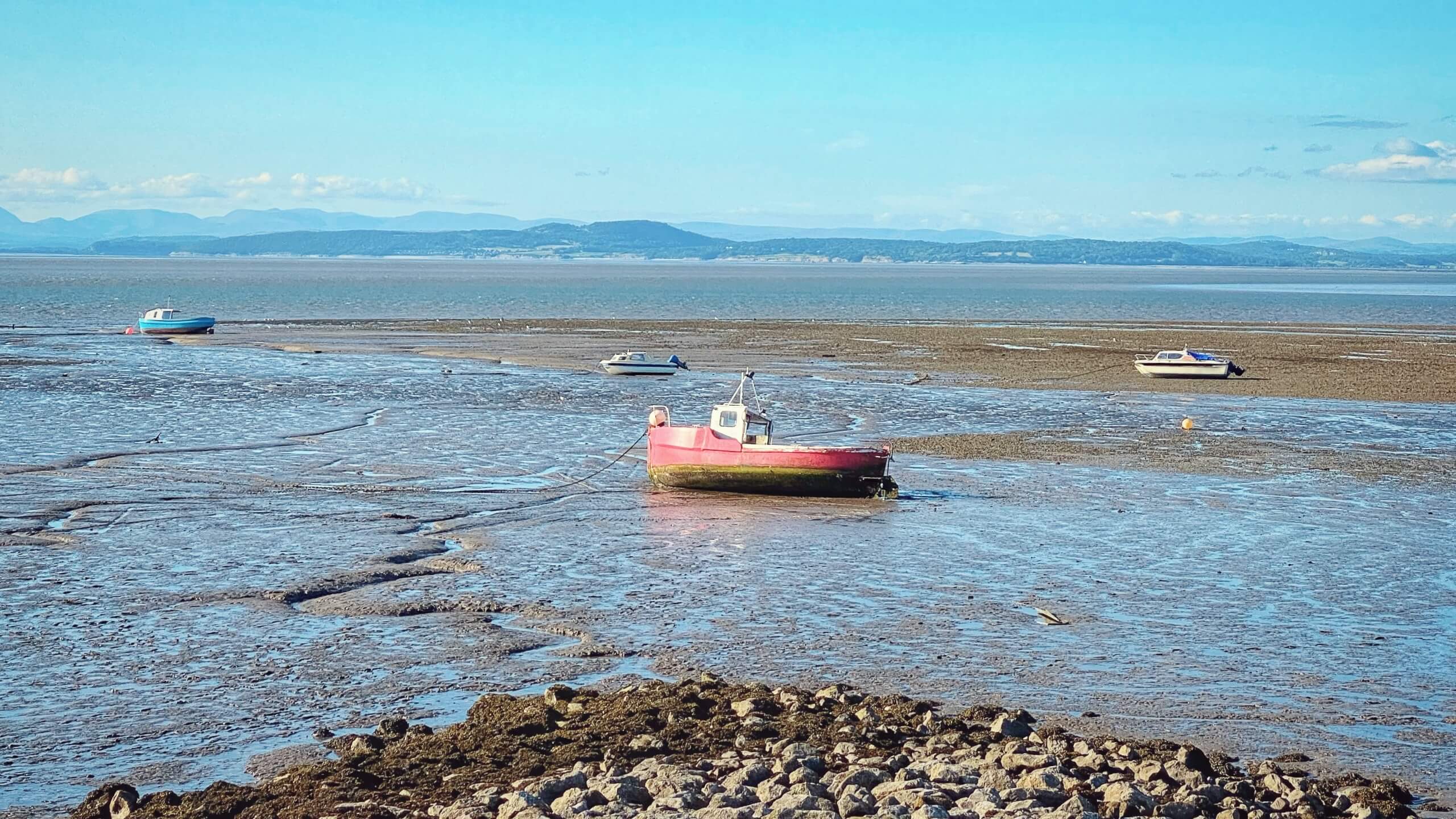 Small fishing boats rest on the sands of Morecambe Bay, with the Lake District hills in the background.