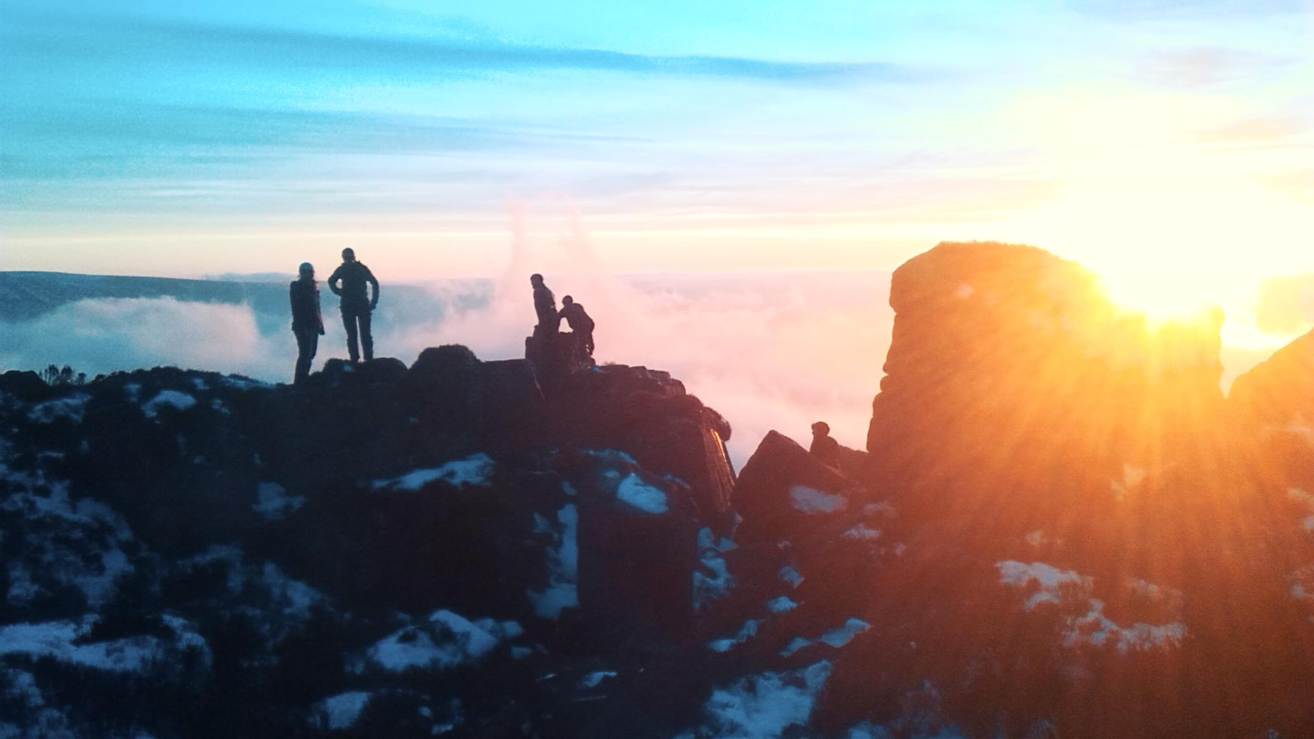 Four students on a craggy, snowy mountain top at dawn in the Lake District.