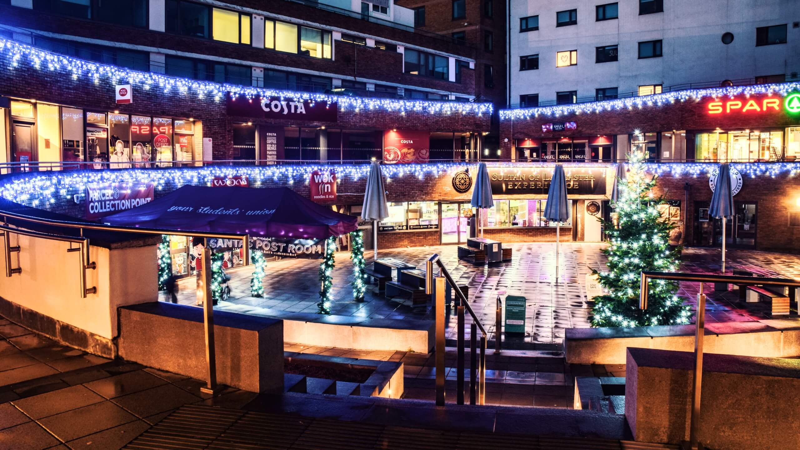 Christmas lights shine across shops in a square