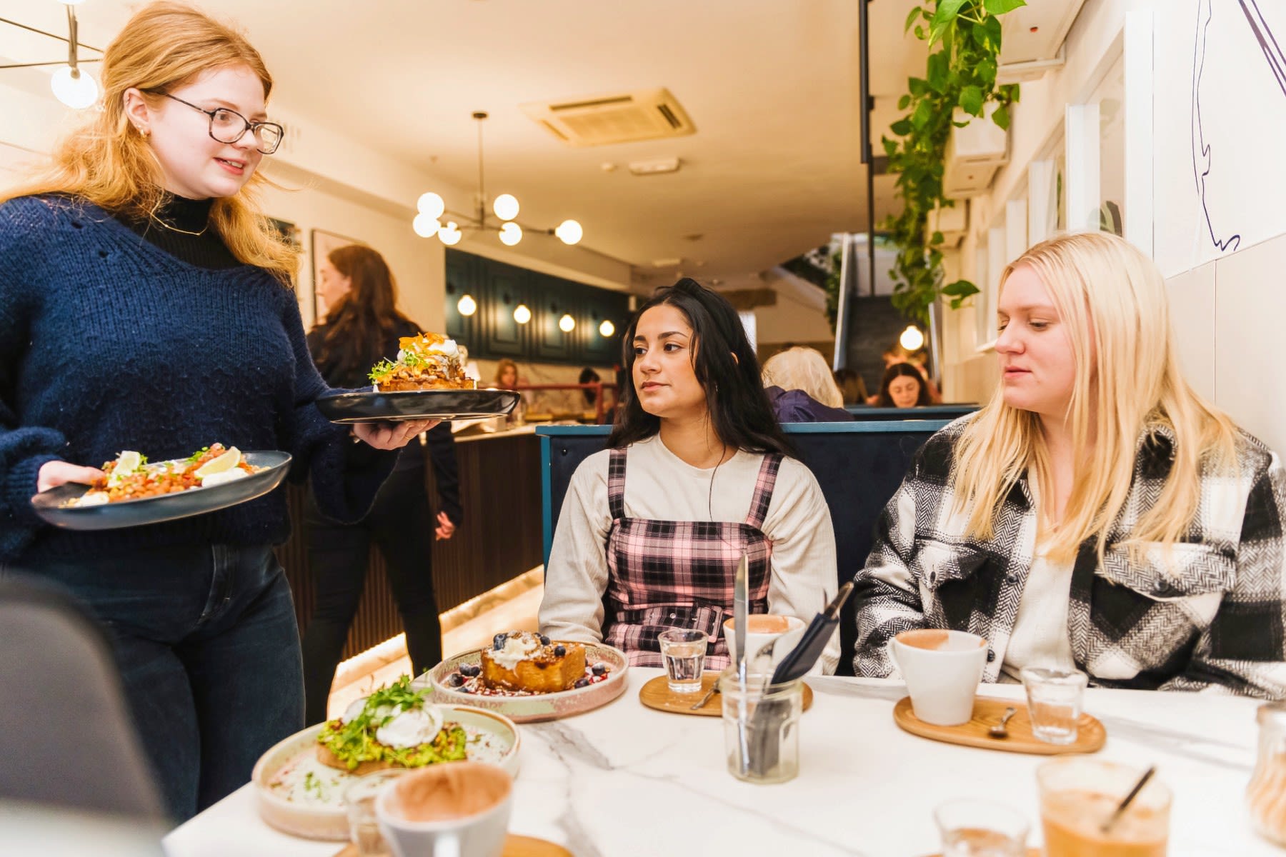 Two female students are served food by wait staff in a brightly lit restaurant.