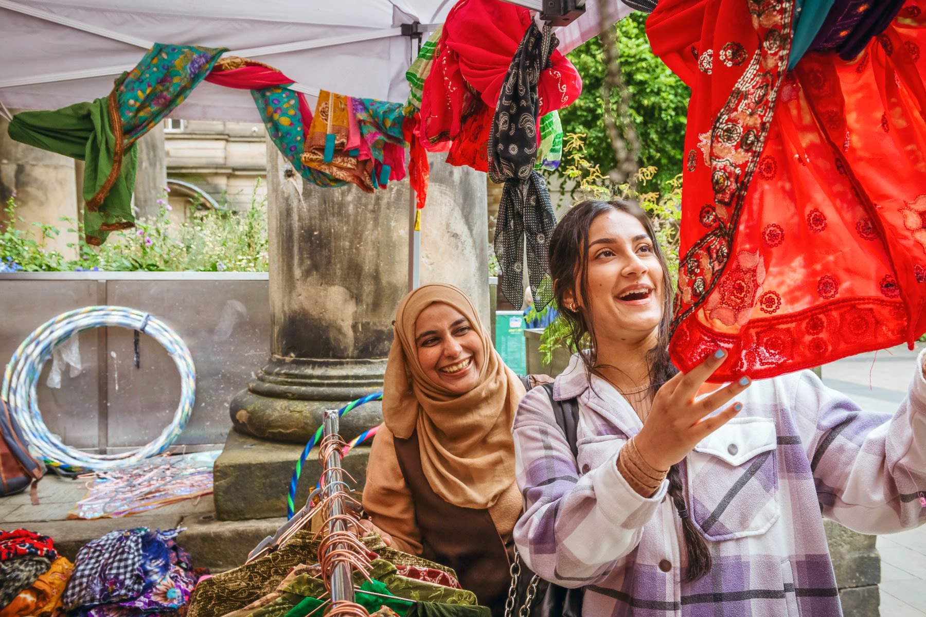 Two students look at brightly coloured fabric on a market stall.