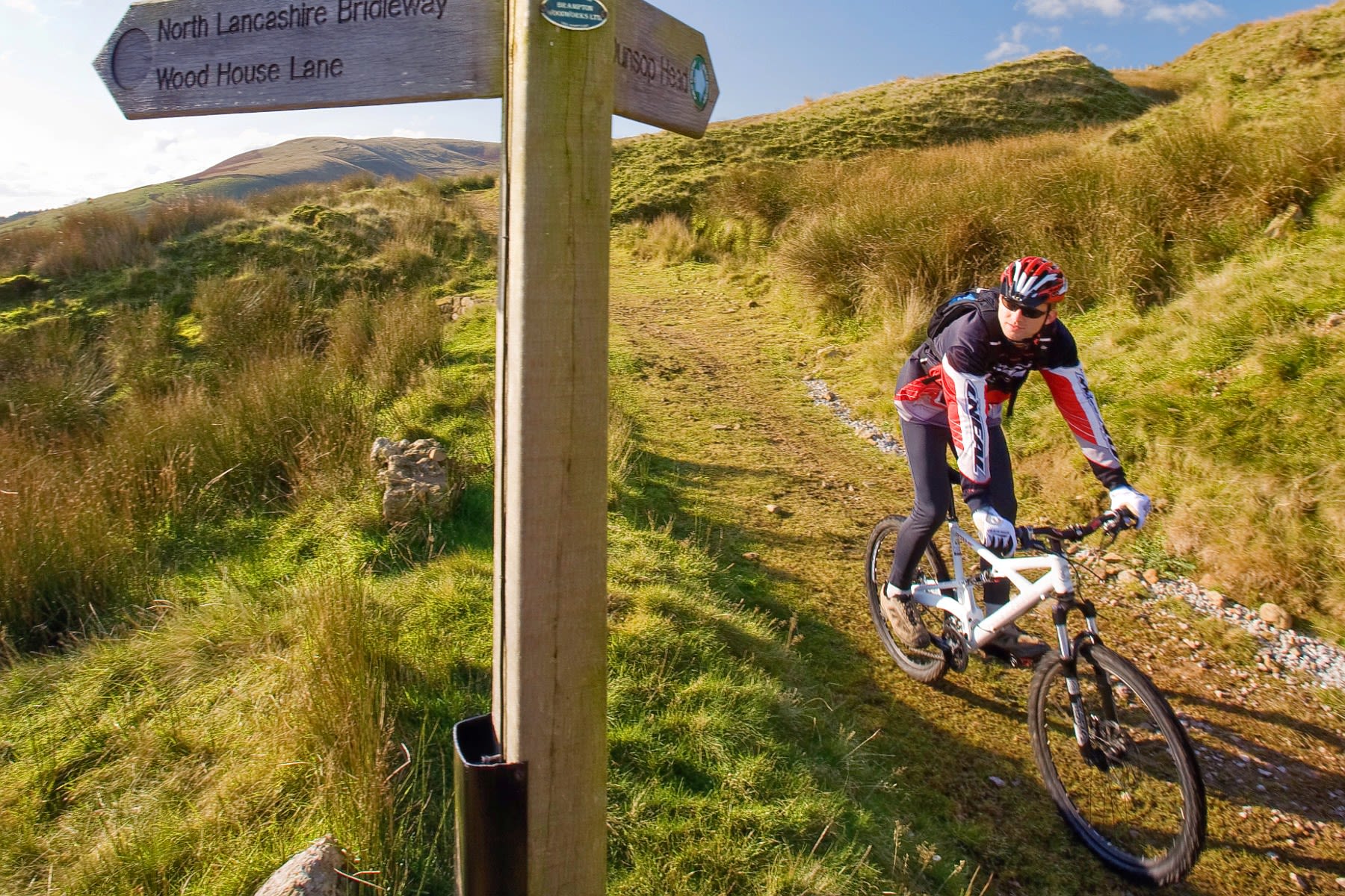 A man on a mountain bike cycles past a signpost on an off-road track.