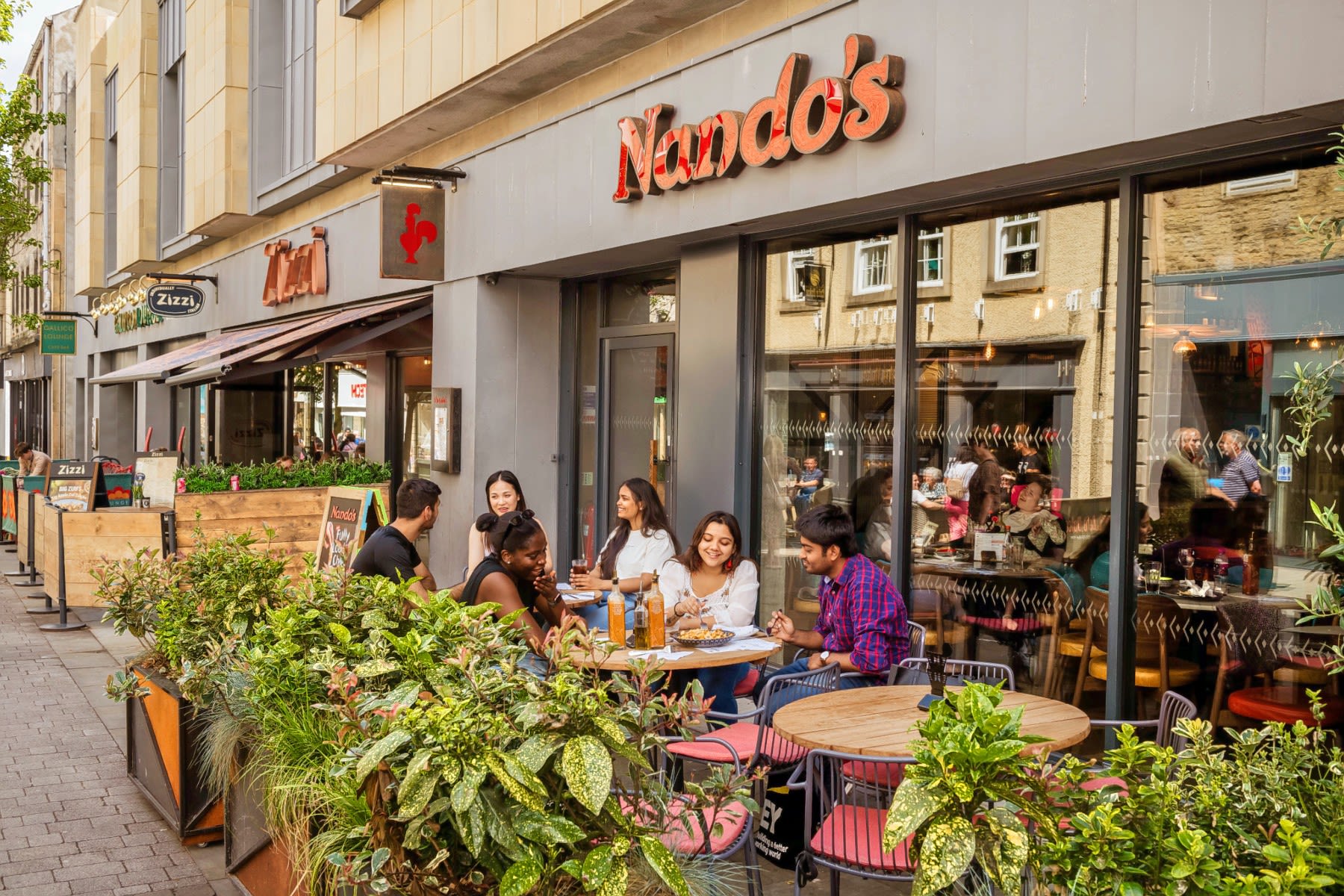Students sit on tables outside a Nando's Restaurant