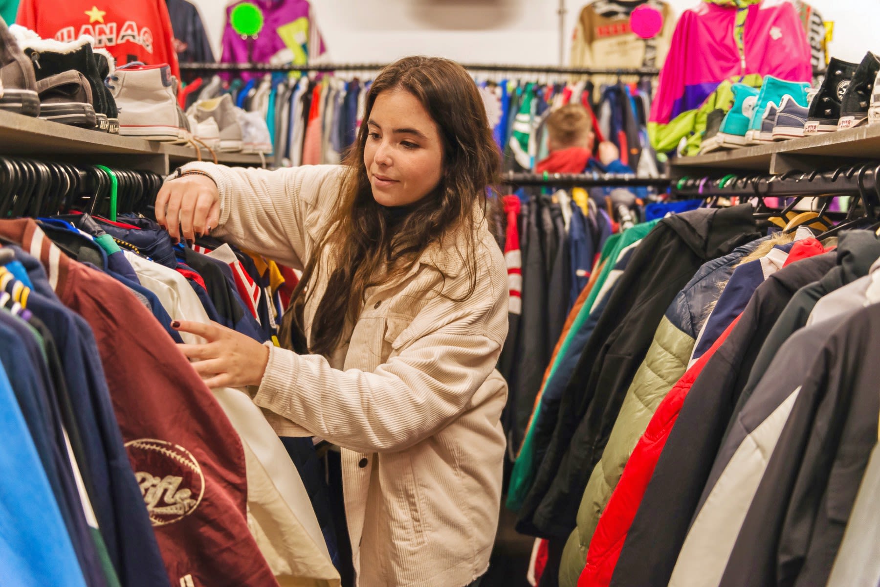 A young woman browses through racks of clothes in a vintage shop.
