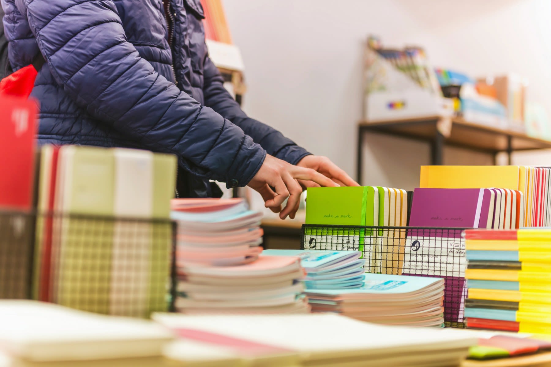 A close up of a pair of hands browsing on a table filled with brightly coloured notebooks.