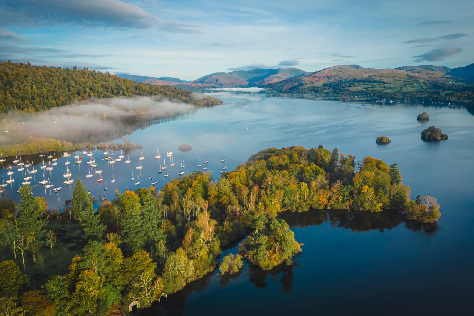 An aerial shot of Windermere showing the lake, forests, boats and mountains.