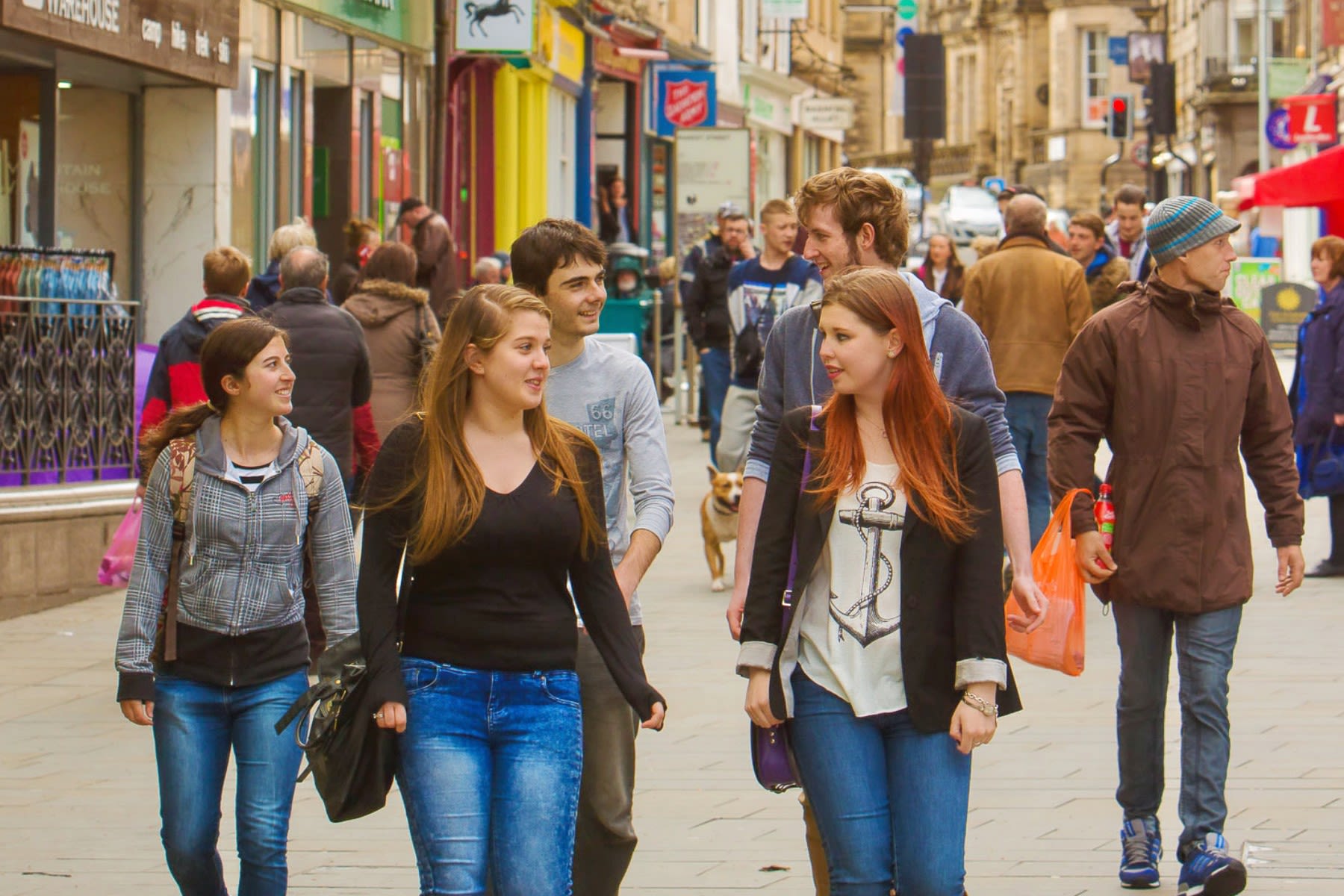 A group of students walk down a busy high street, chatting.