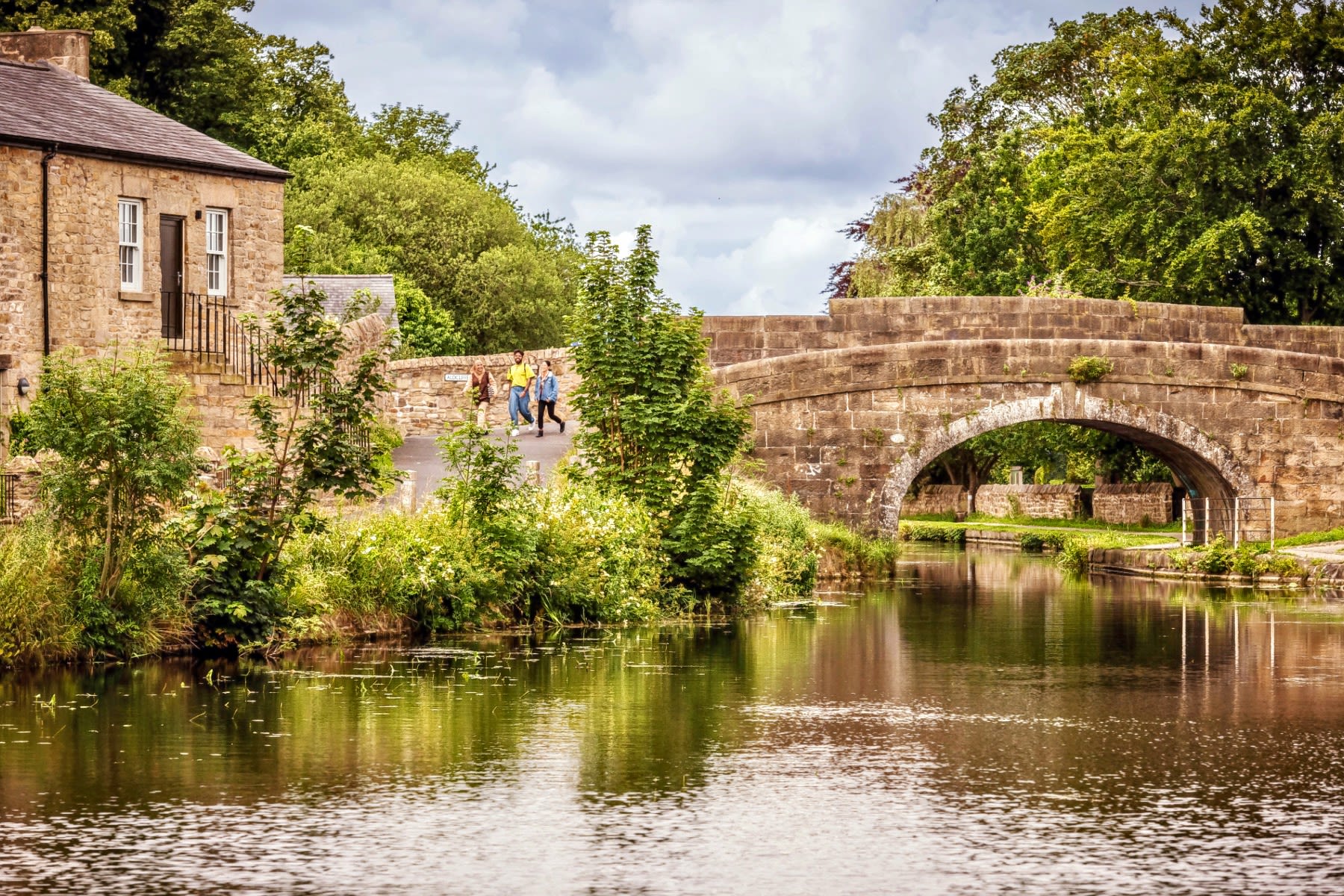 Students go for a walk by a historic canal with a stone bridge and buildings.