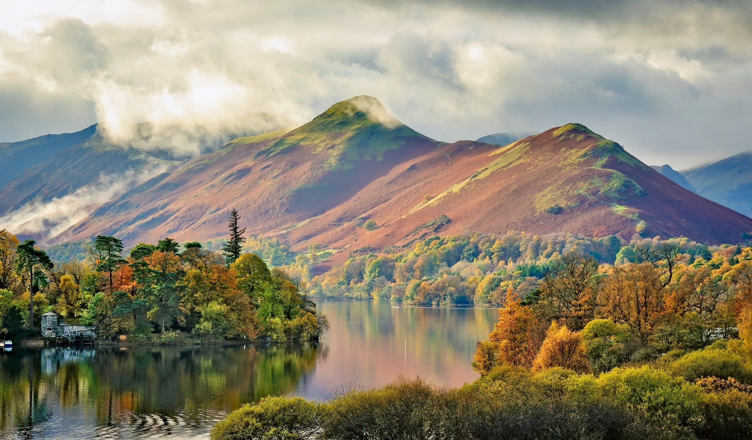 An Autumnal view of woods, lake and mountains in the Lake District.
